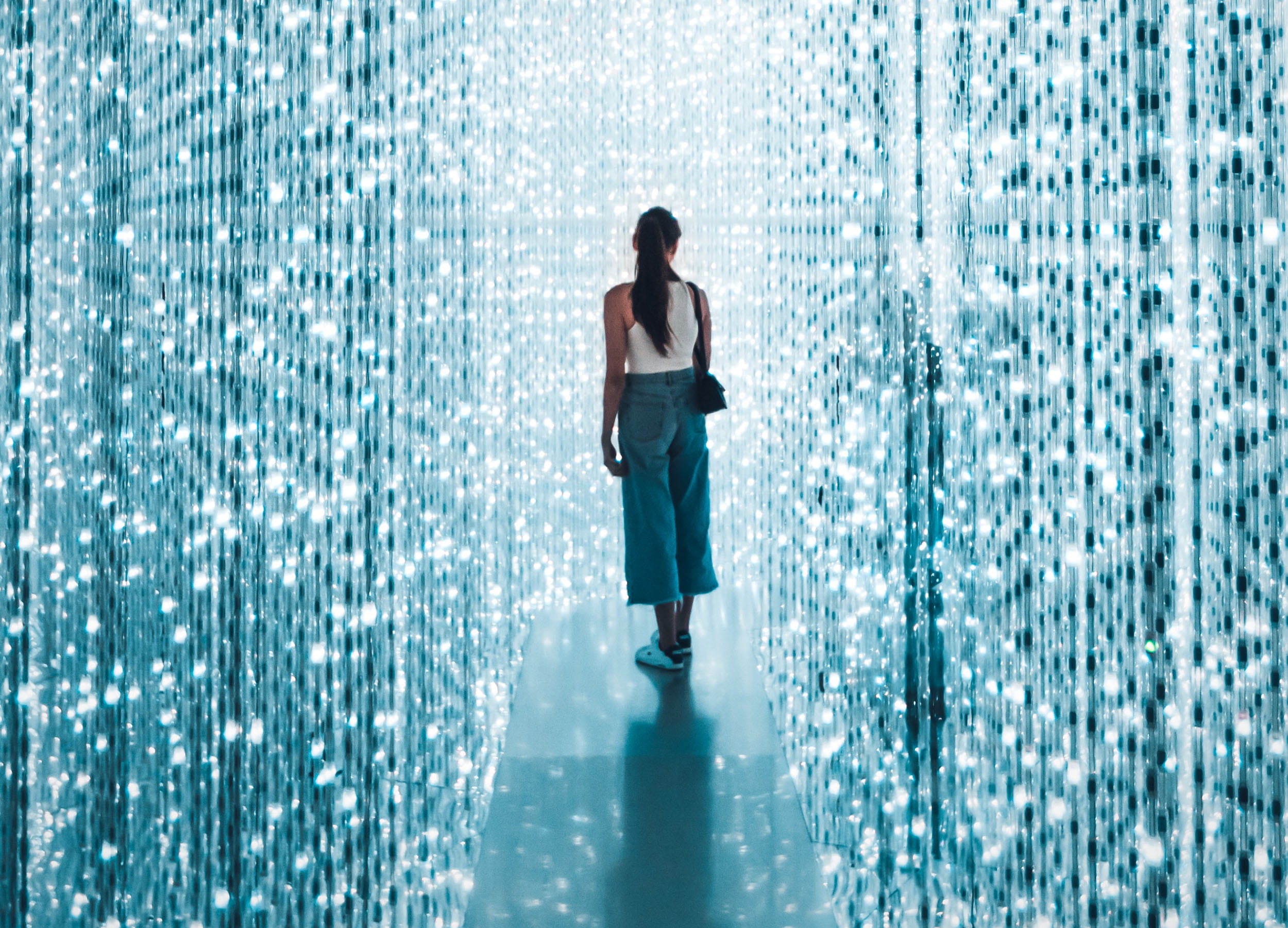 A woman standing on a small platform, surrounded by strings of blue and white lights running floor to ceiling.